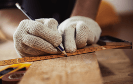 Person in work gloves using a pencil and ruler to measure and mark wood.
