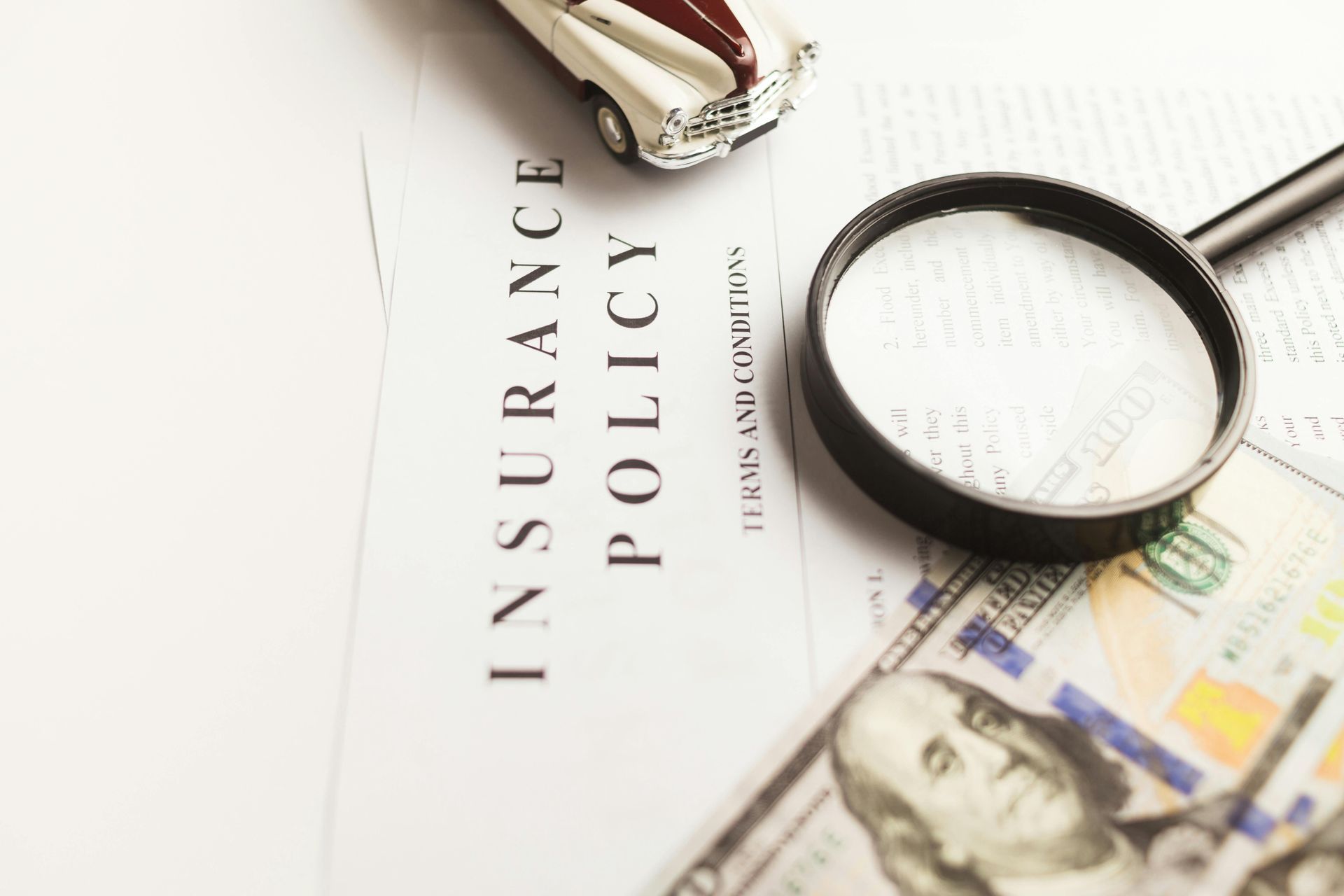Insurance policy with toy car, magnifying glass, and cash, illustrating policy review.