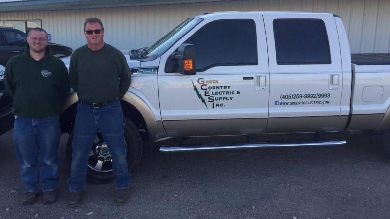 Two people stand smiling next to a white pickup truck with 