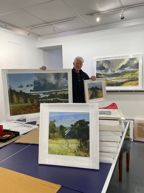 A man is holding two framed paintings on a table