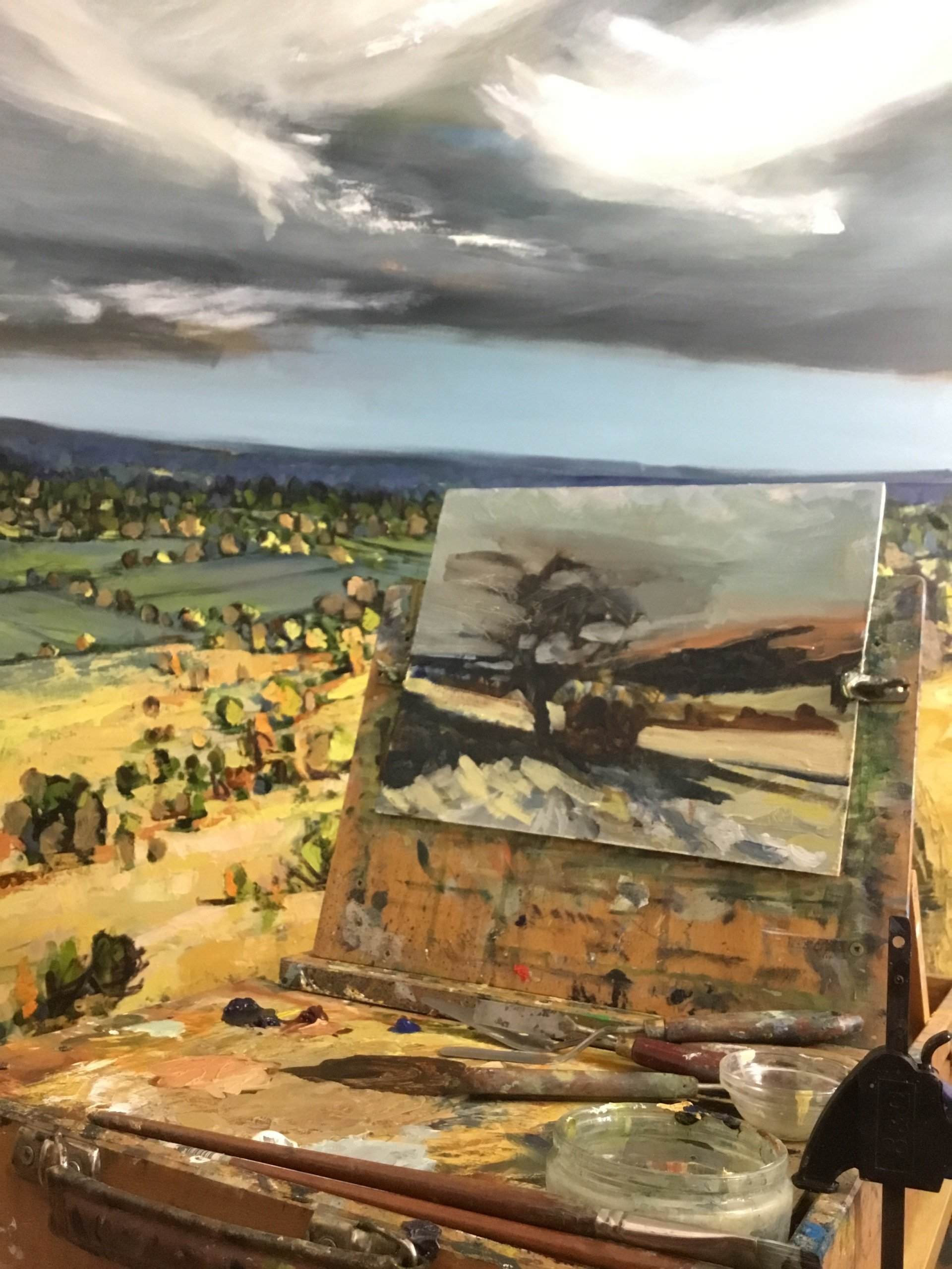 A painting is being painted on an easel in front of a large painting.