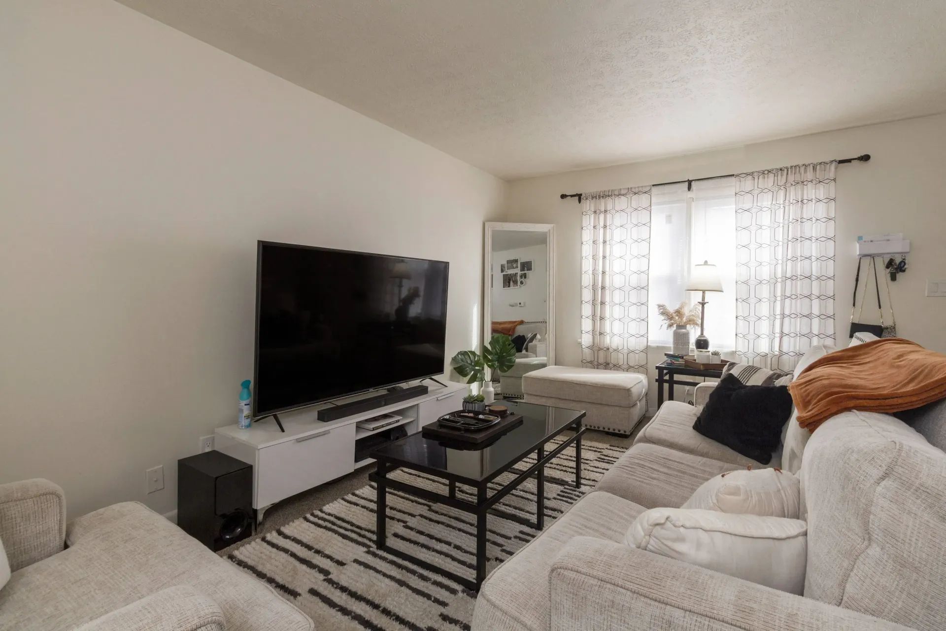 Living room with a large TV, white couch, black coffee table, and patterned rug.