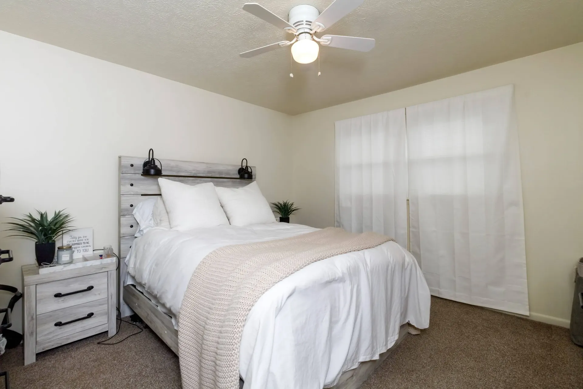 Bedroom with white walls, bed, nightstand, and sheer curtains.