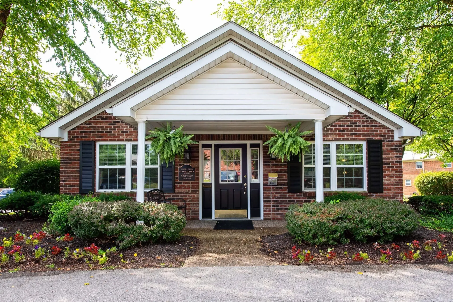 Brick building with black door, white trim, hanging plants, and bushes.