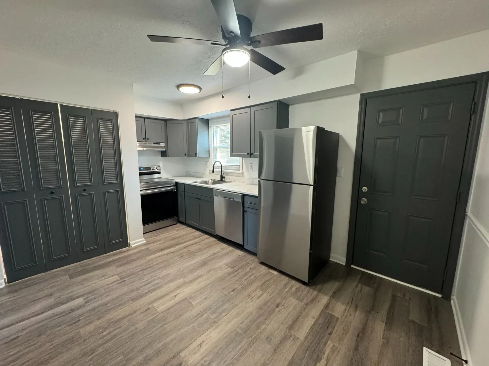 Gray-painted kitchen with stainless steel appliances, gray cabinets, and a dark gray door.