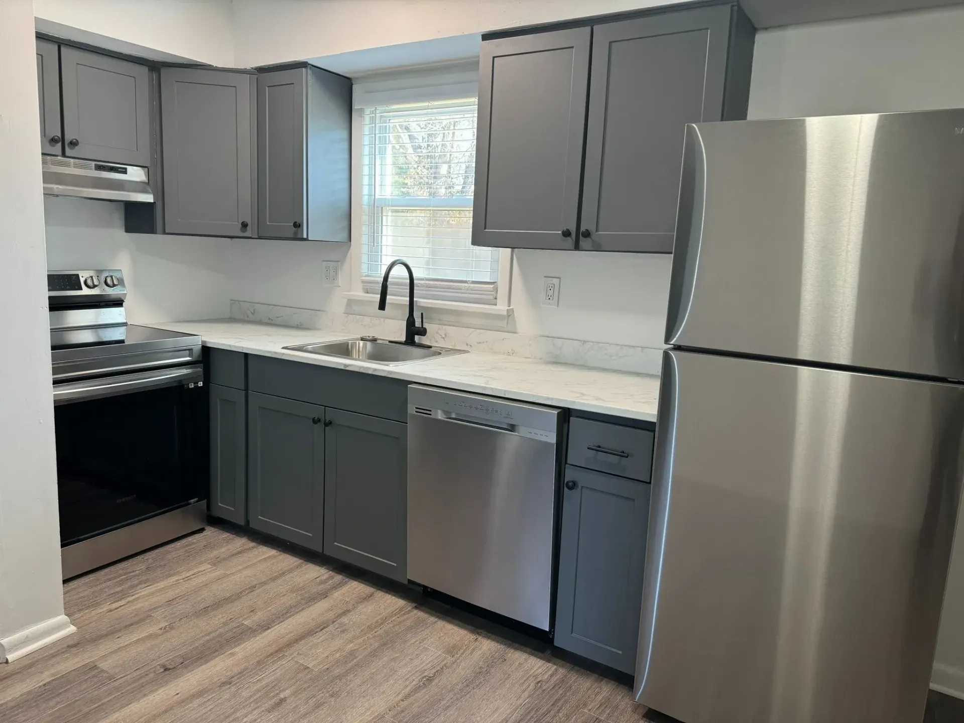 Modern kitchen with grey cabinets, stainless steel appliances, and white countertops.