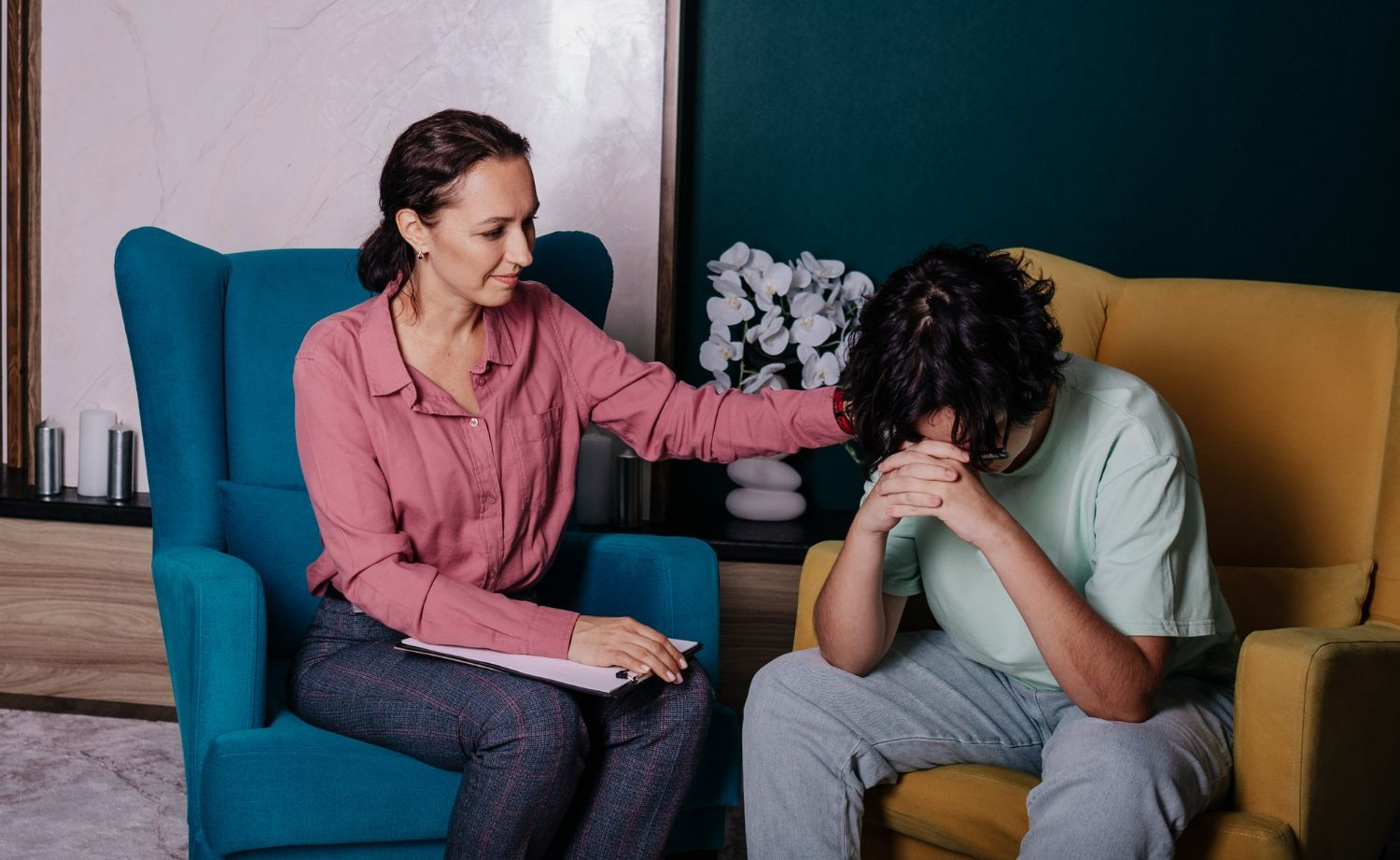 A woman is sitting in a chair talking to a man who is sitting in a chair with his head down.
