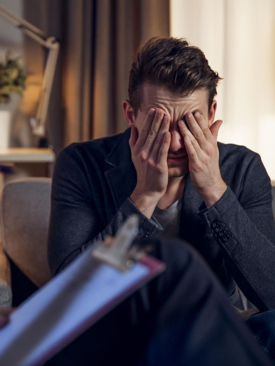 a man is sitting in a chair covering his eyes with his hands .