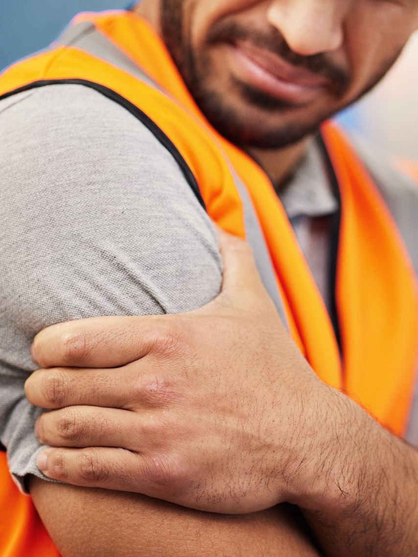 a man in an orange vest is holding his arm in pain .