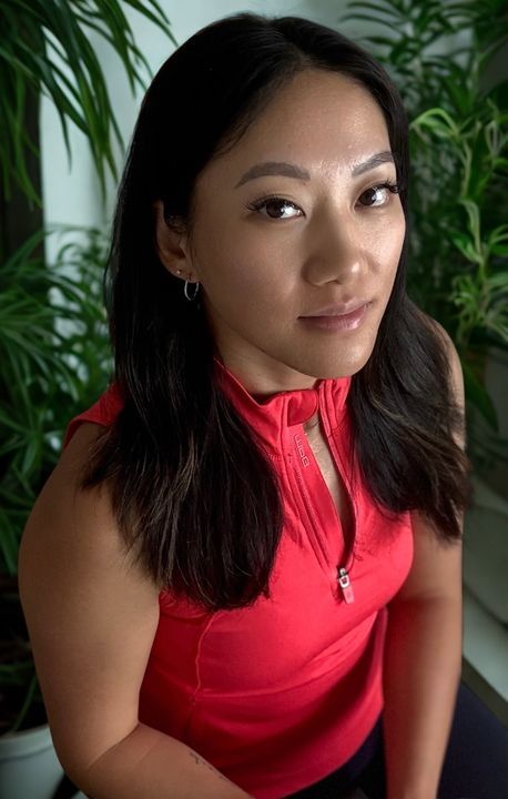 A woman in a red shirt is sitting in front of a plant.