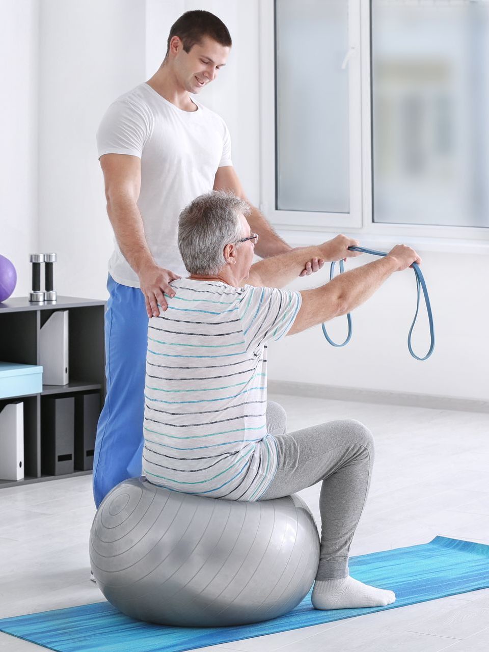a man is sitting on an exercise ball while a man stands behind him .
