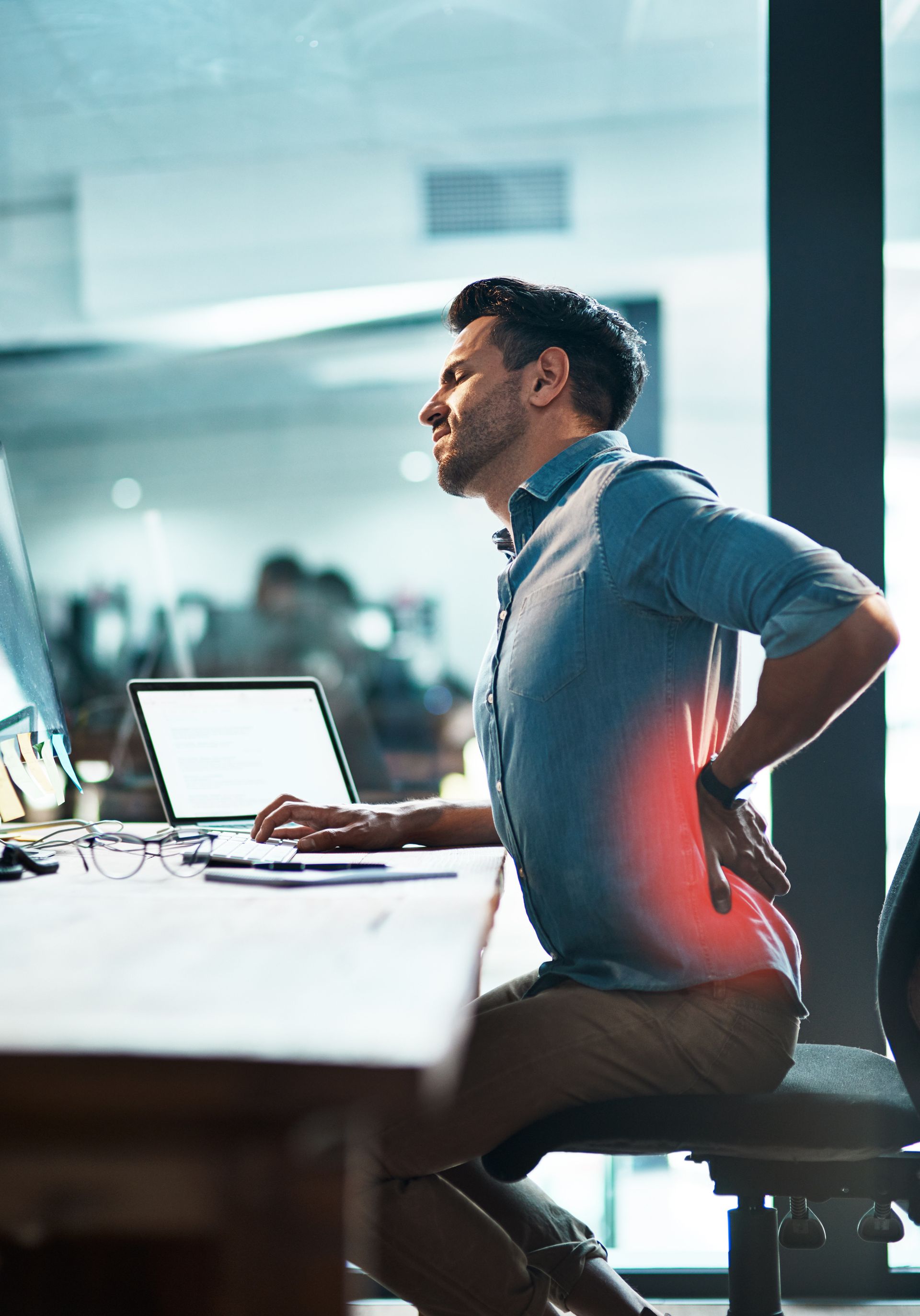 a man is sitting at a desk holding his back in pain .