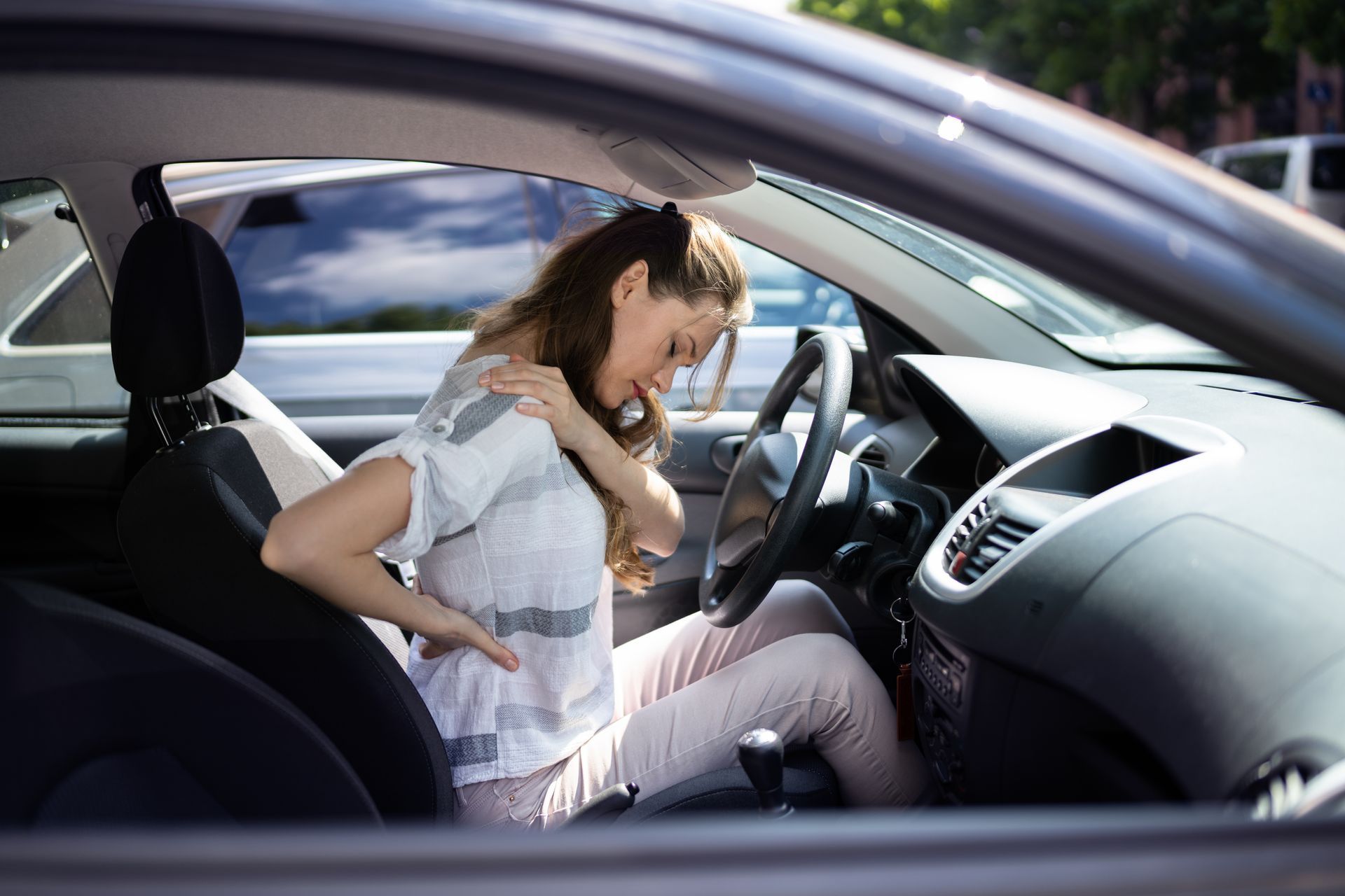 Woman wincing with back and shoulder pain while sitting in her car.
