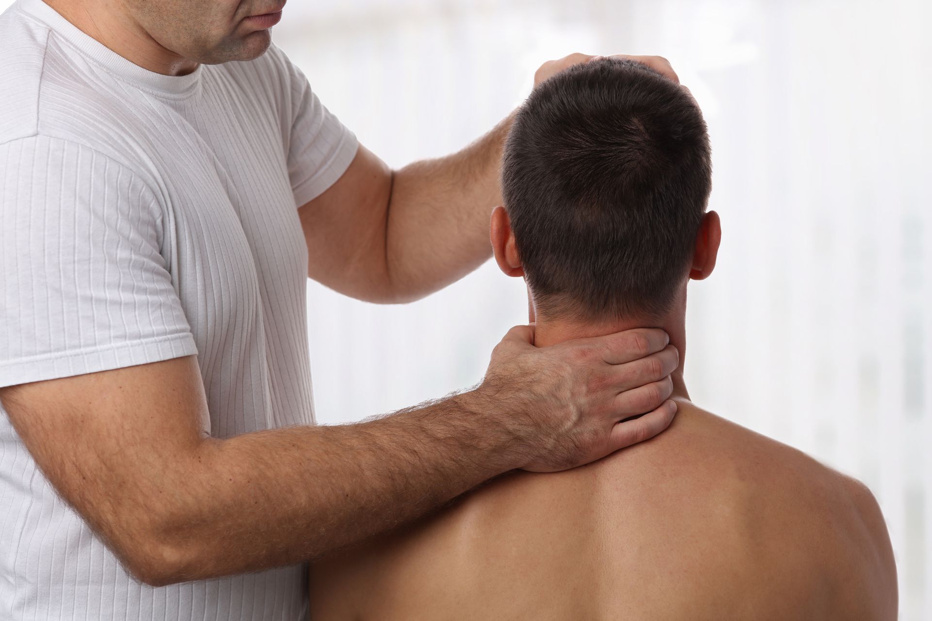 Therapist performing a neck adjustment on a seated man.