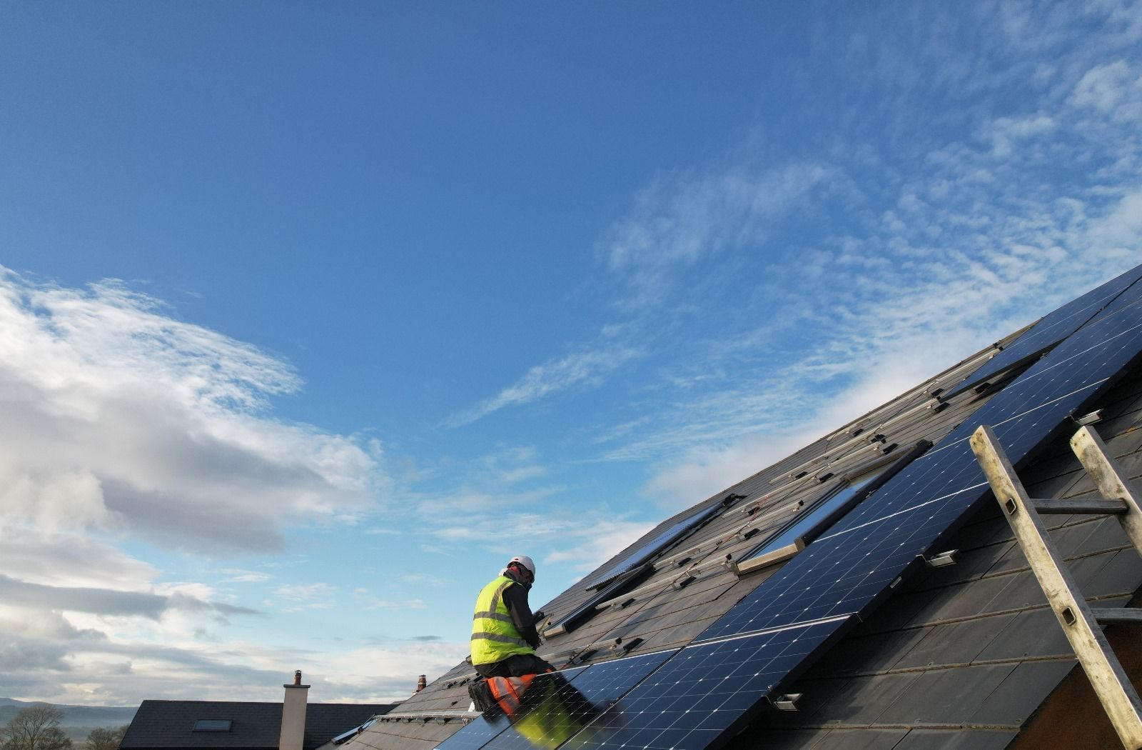 A man is installing solar panels on the roof of a house.