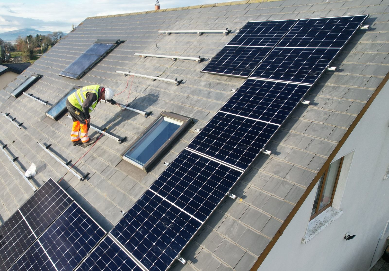 A man is installing solar panels on the roof of a house