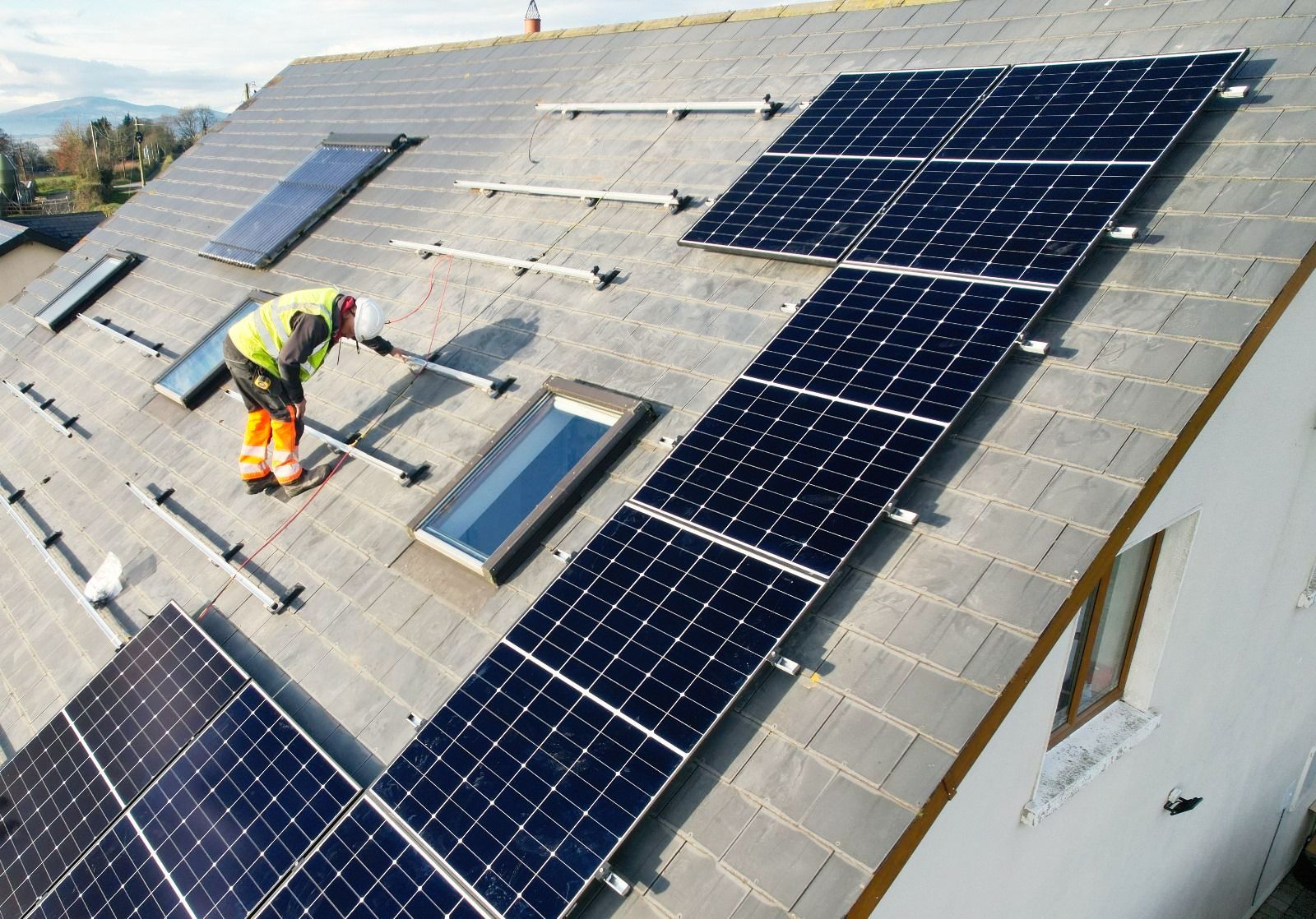 A man is installing solar panels on the roof of a house