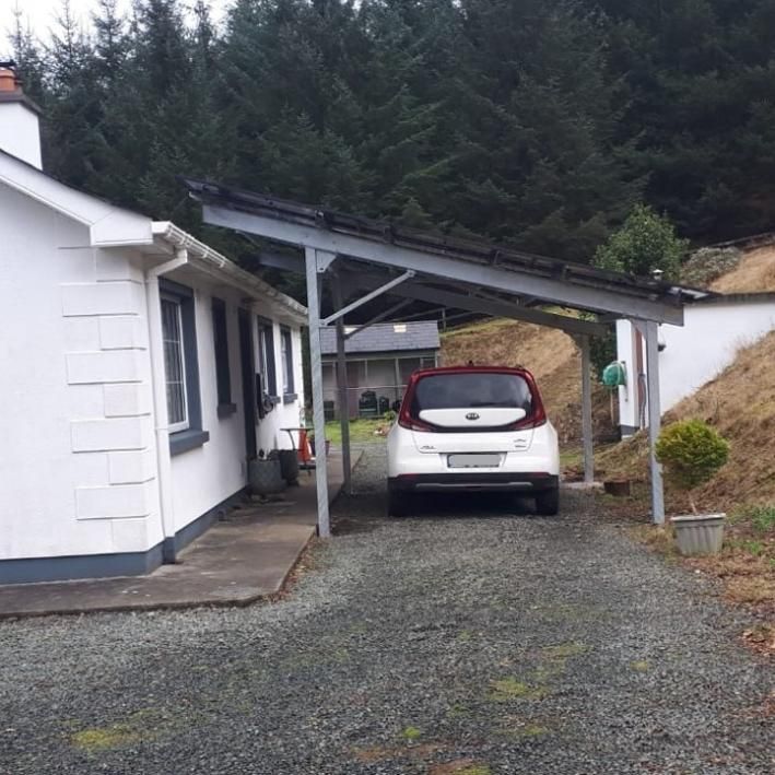 A car is parked under a canopy in front of a white house
