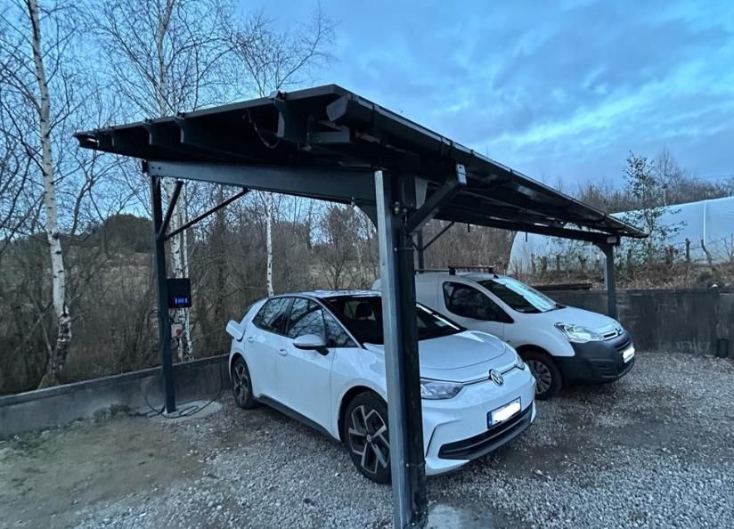 Two electric cars are parked under a carport.