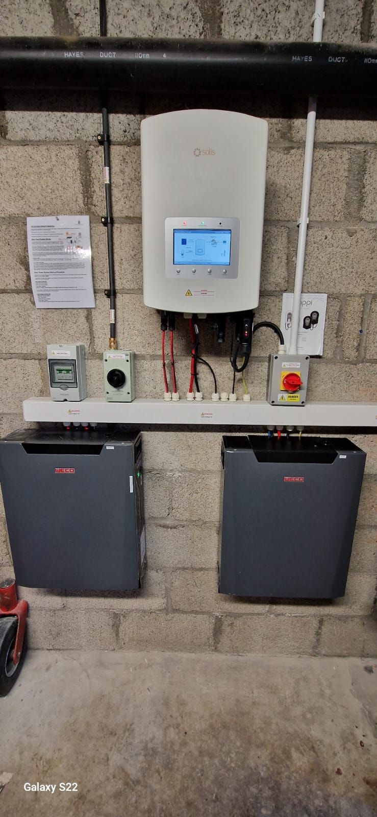 A solar panel is mounted on a brick wall next to two batteries.