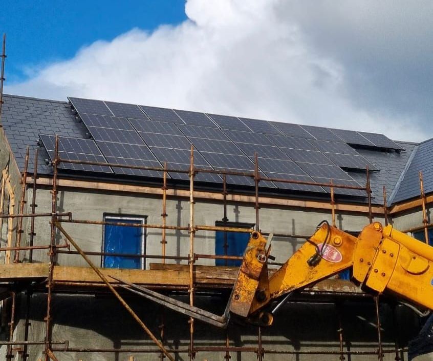 A yellow forklift is working on a building with solar panels on the roof