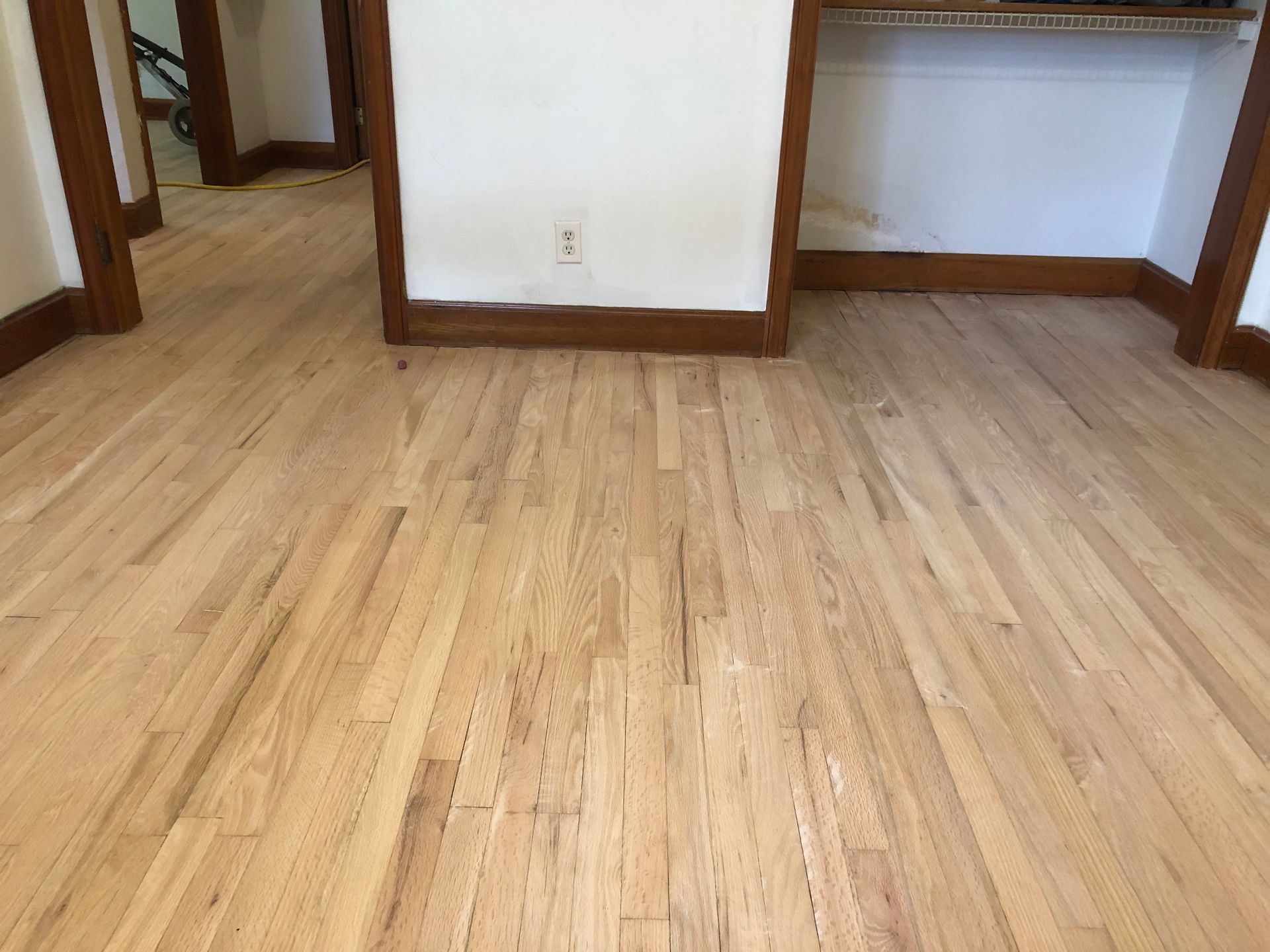 A room with a sanded wooden floor and a white wall.