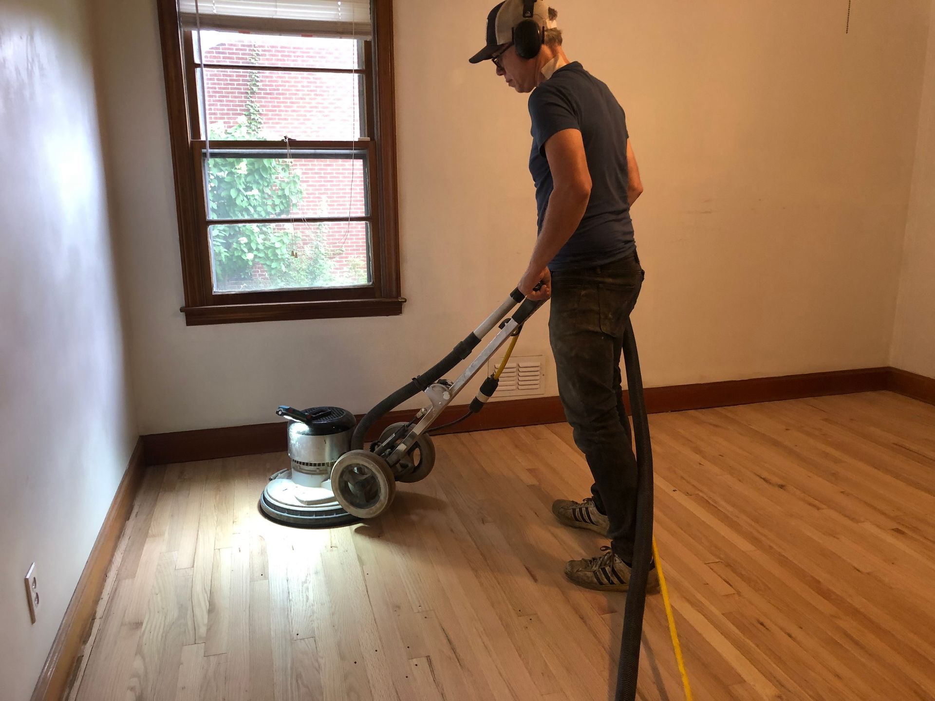 A man is sanding a wooden floor with a sanding machine.