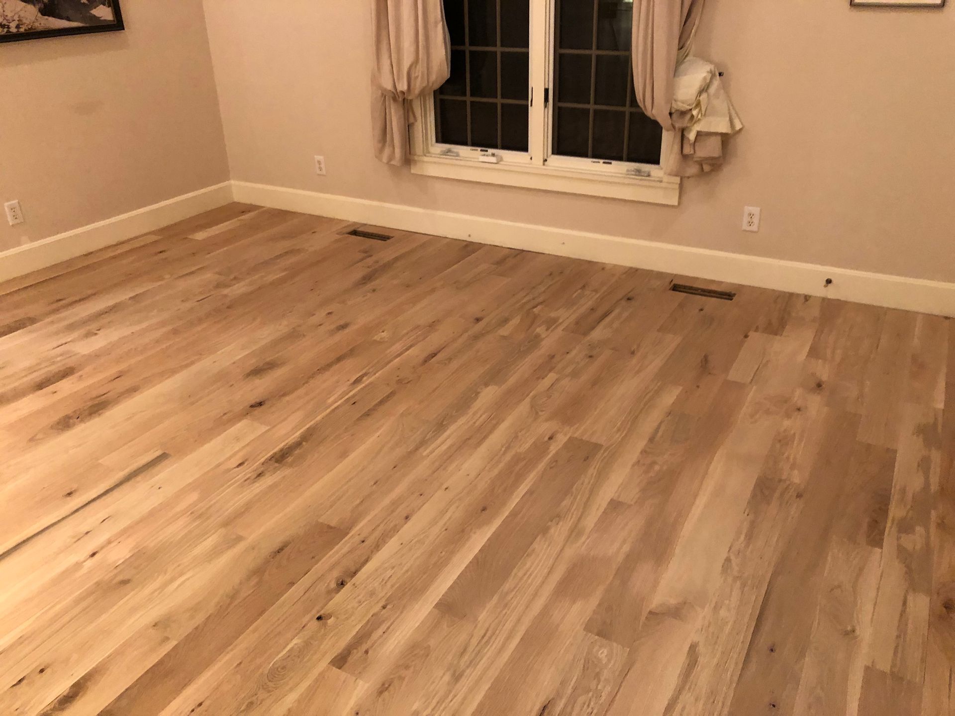 A bedroom with hardwood floors and a window.