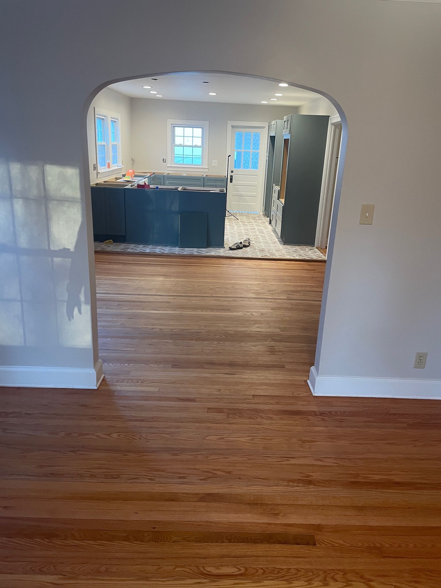 View through an arched doorway into a kitchen with blue cabinets, white walls, and wooden floors.
