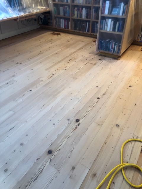A wooden floor in a room with bookshelves and a yellow cord.