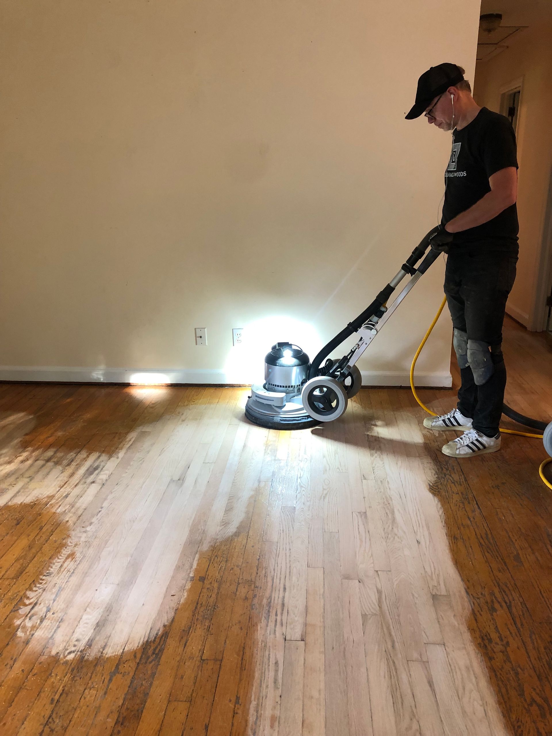 A man is sanding a wooden floor with a floor sanding machine.