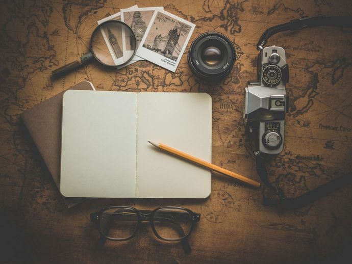 A notebook , camera , magnifying glass , glasses and a pencil on a map.Wide