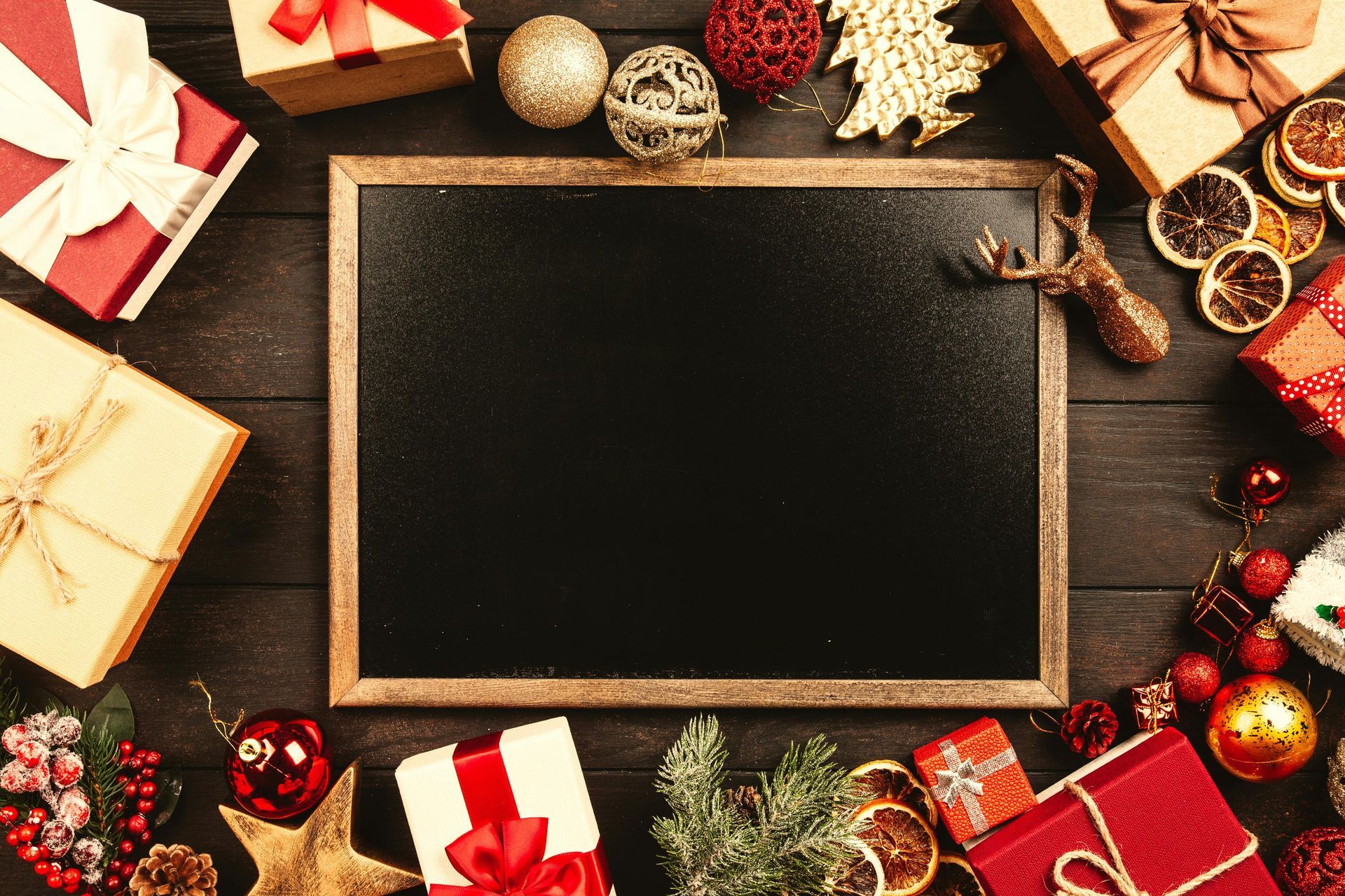 A blackboard is surrounded by christmas decorations and gifts on a wooden table.