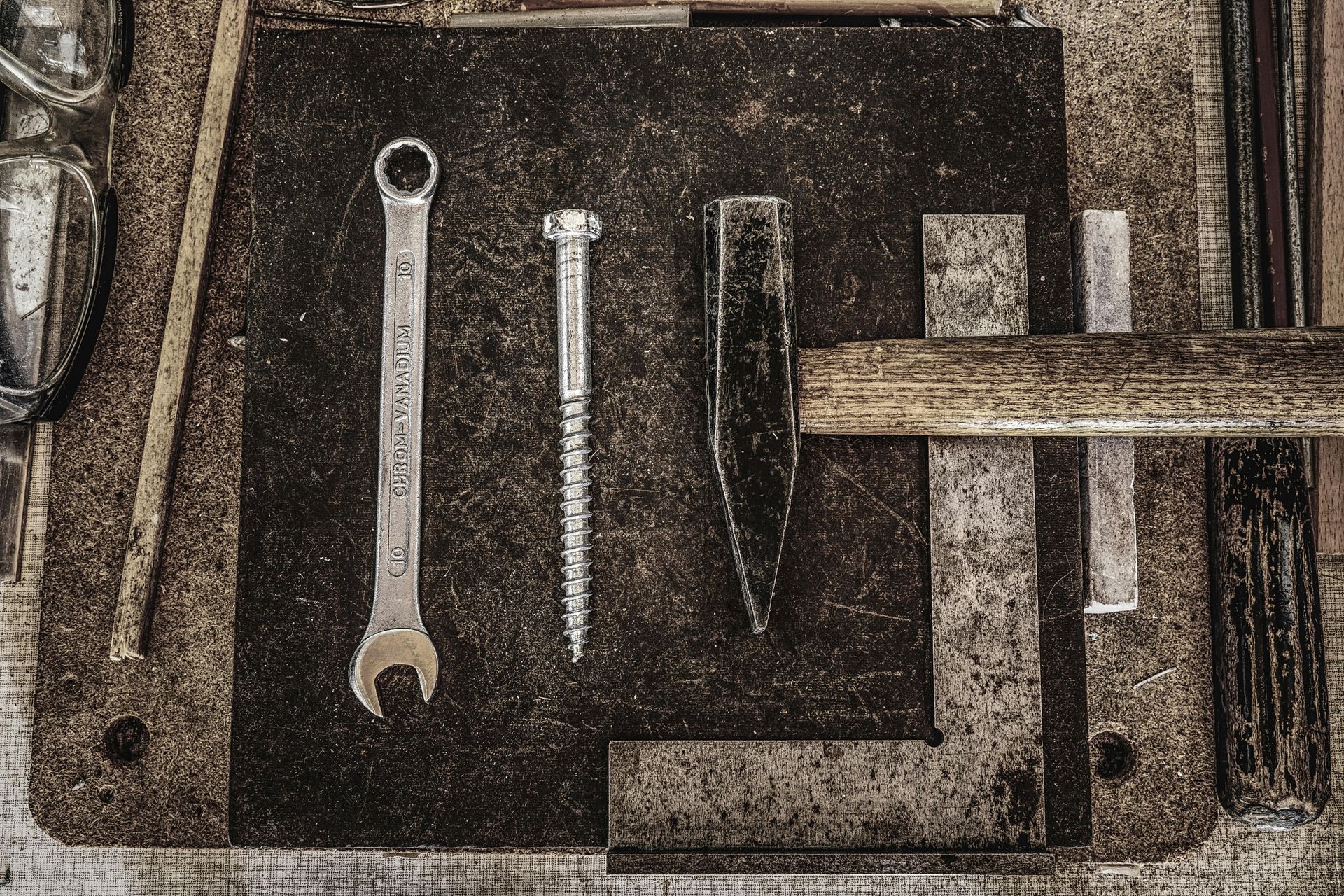A wrench , screws , and a hammer are on a wooden table.