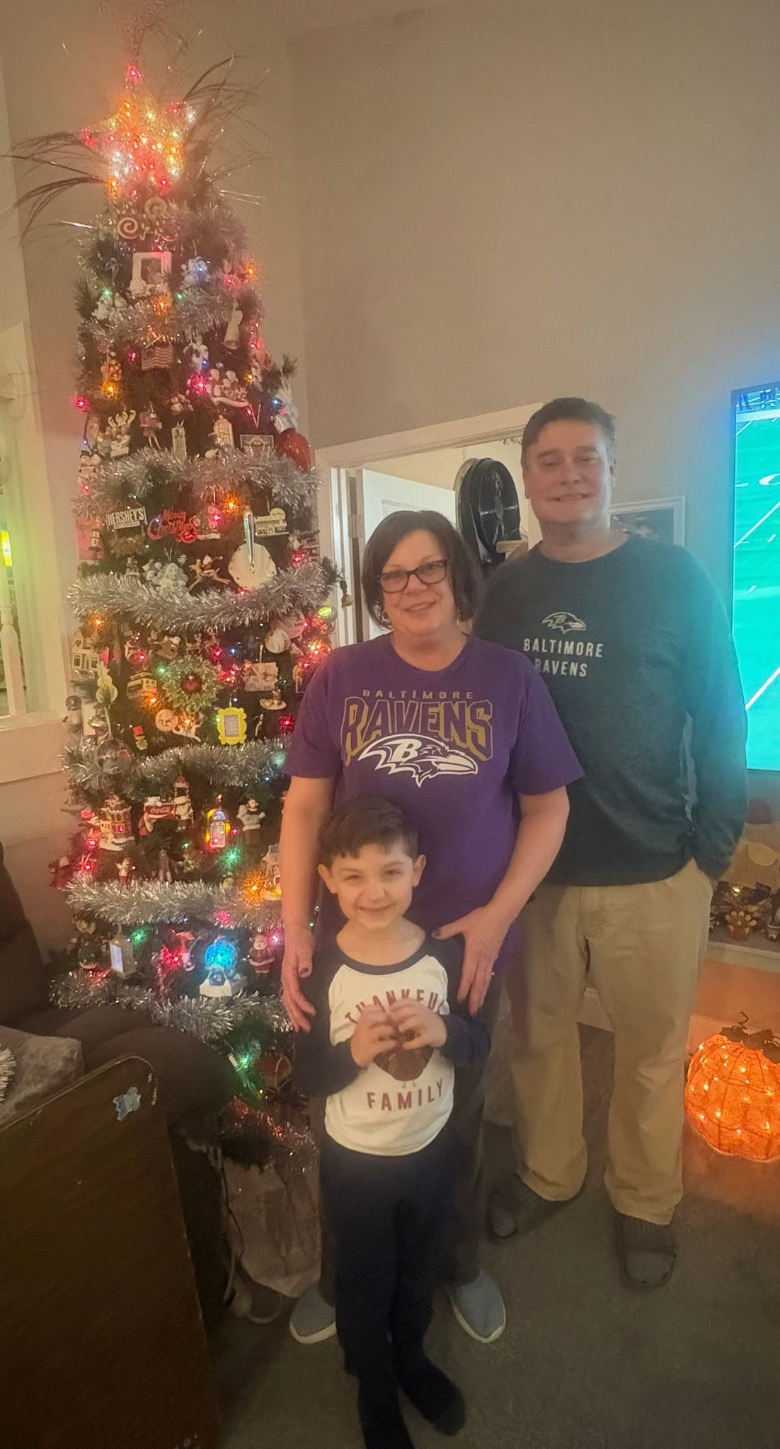 Family of three poses in front of a Christmas tree with colorful lights.