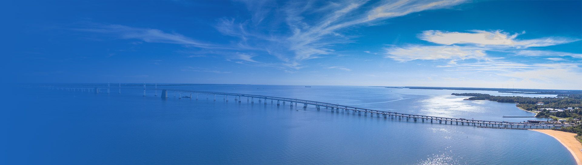 Aerial view of a long bridge over a wide body of water, under a bright blue sky.