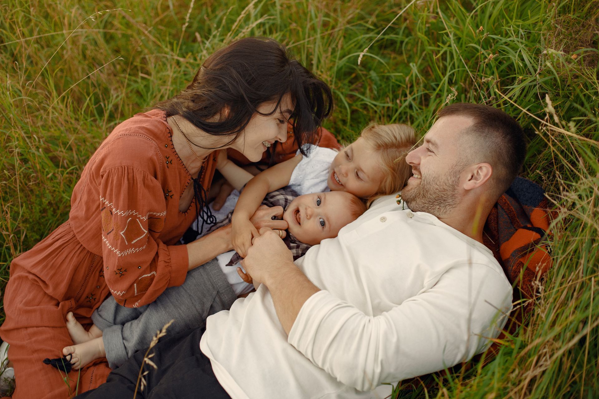 Family laughing and embracing in tall grass, enjoying a sunny day.