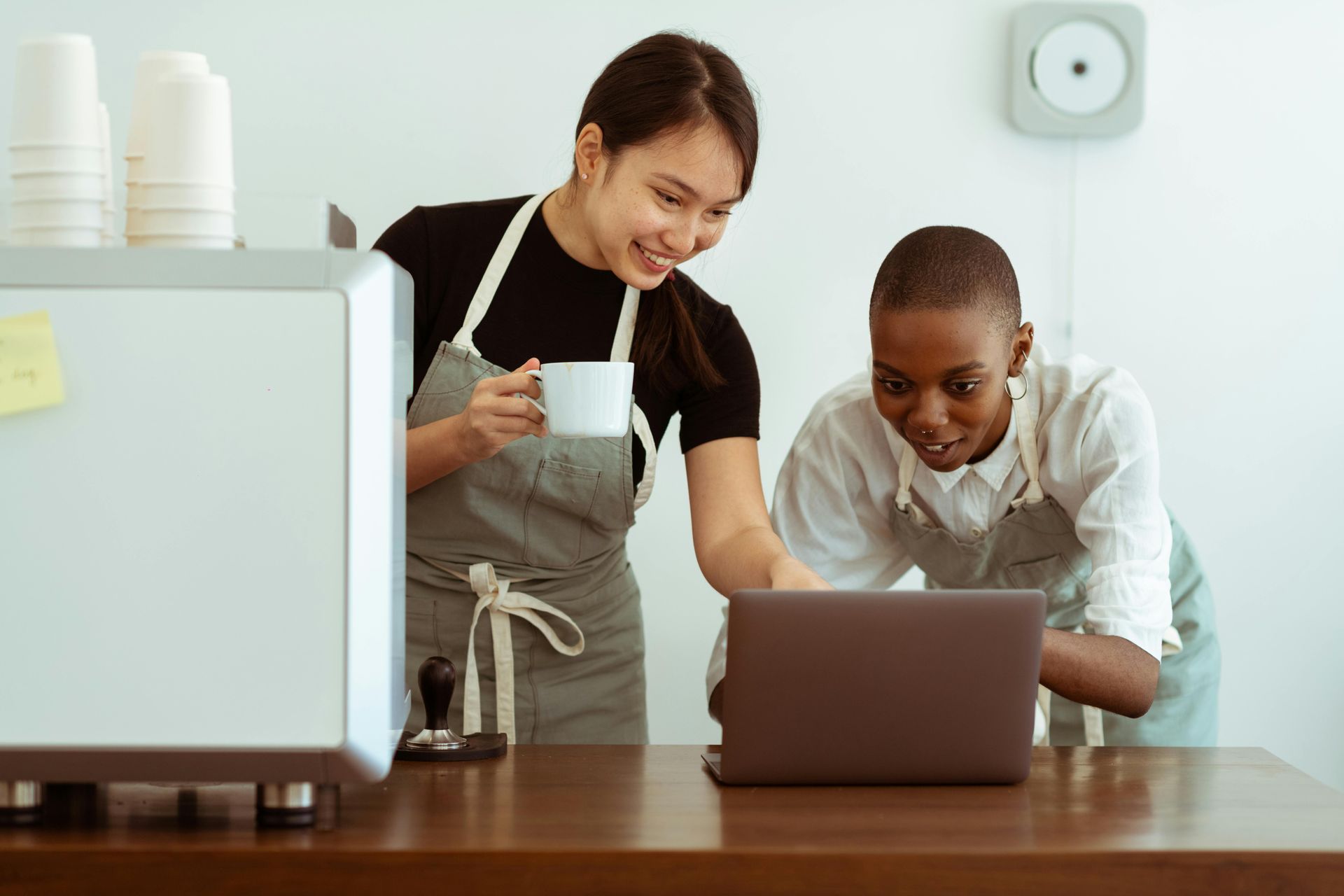 Two cafe workers looking at a laptop, one holding a mug.