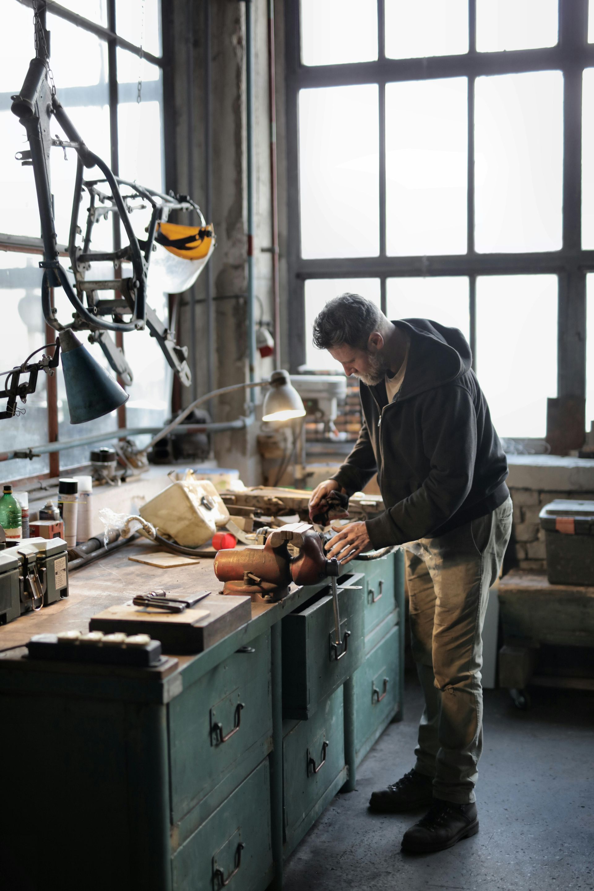 Man working on workbench in workshop. Window, tools, metal object.