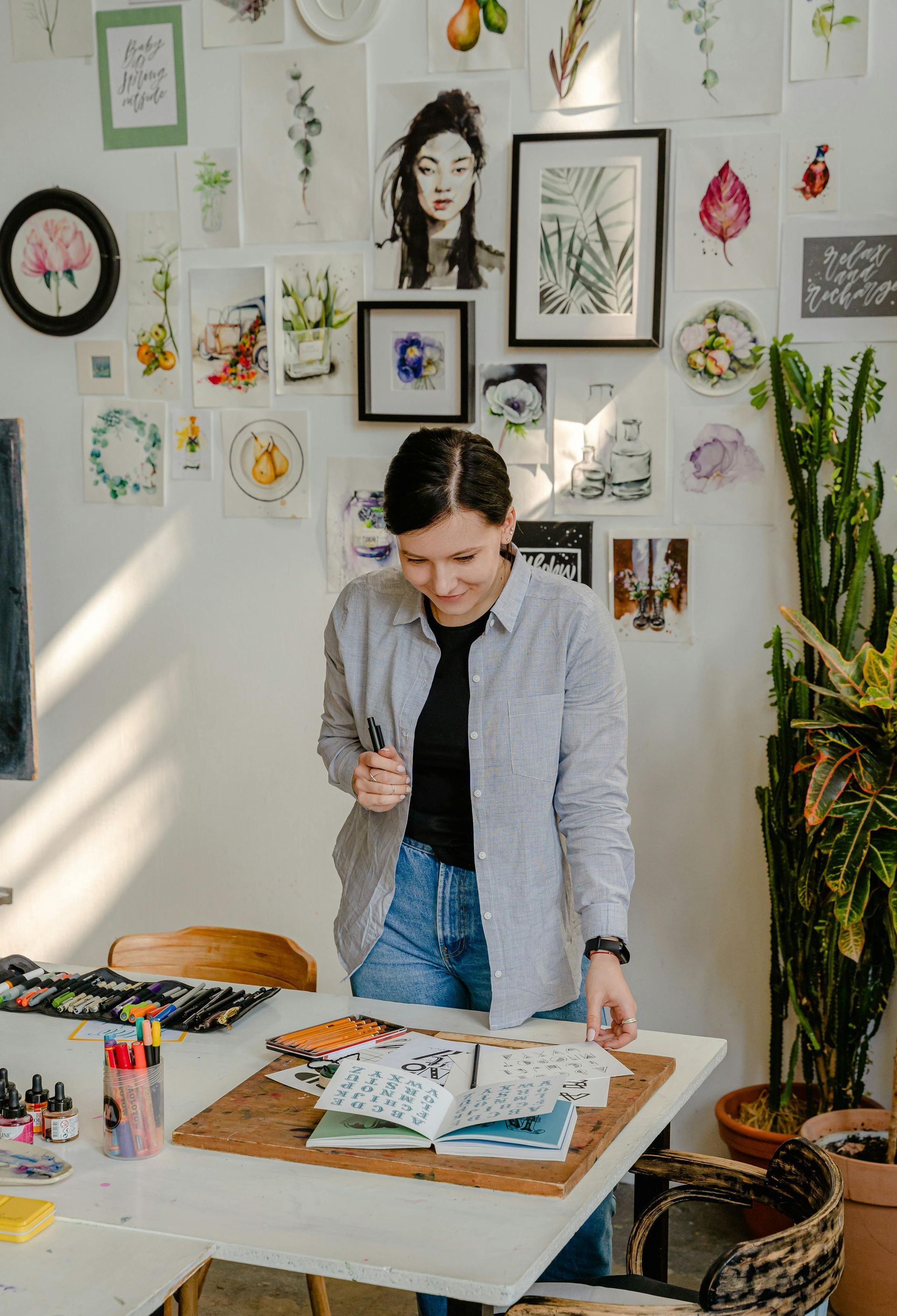 Woman in art studio looking at sketches, surrounded by artwork.
