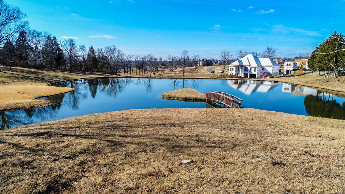 A small bridge over a pond with a house in the background.