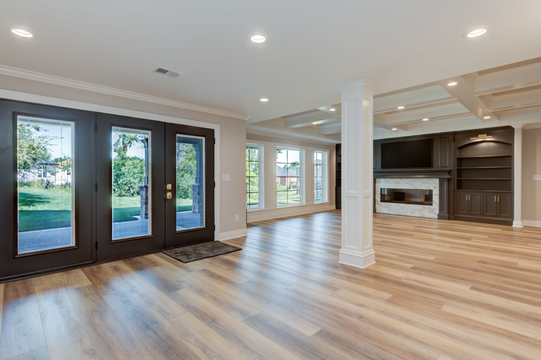 Spacious living area with French doors, light wood floors, built-in entertainment center, and recessed lighting.