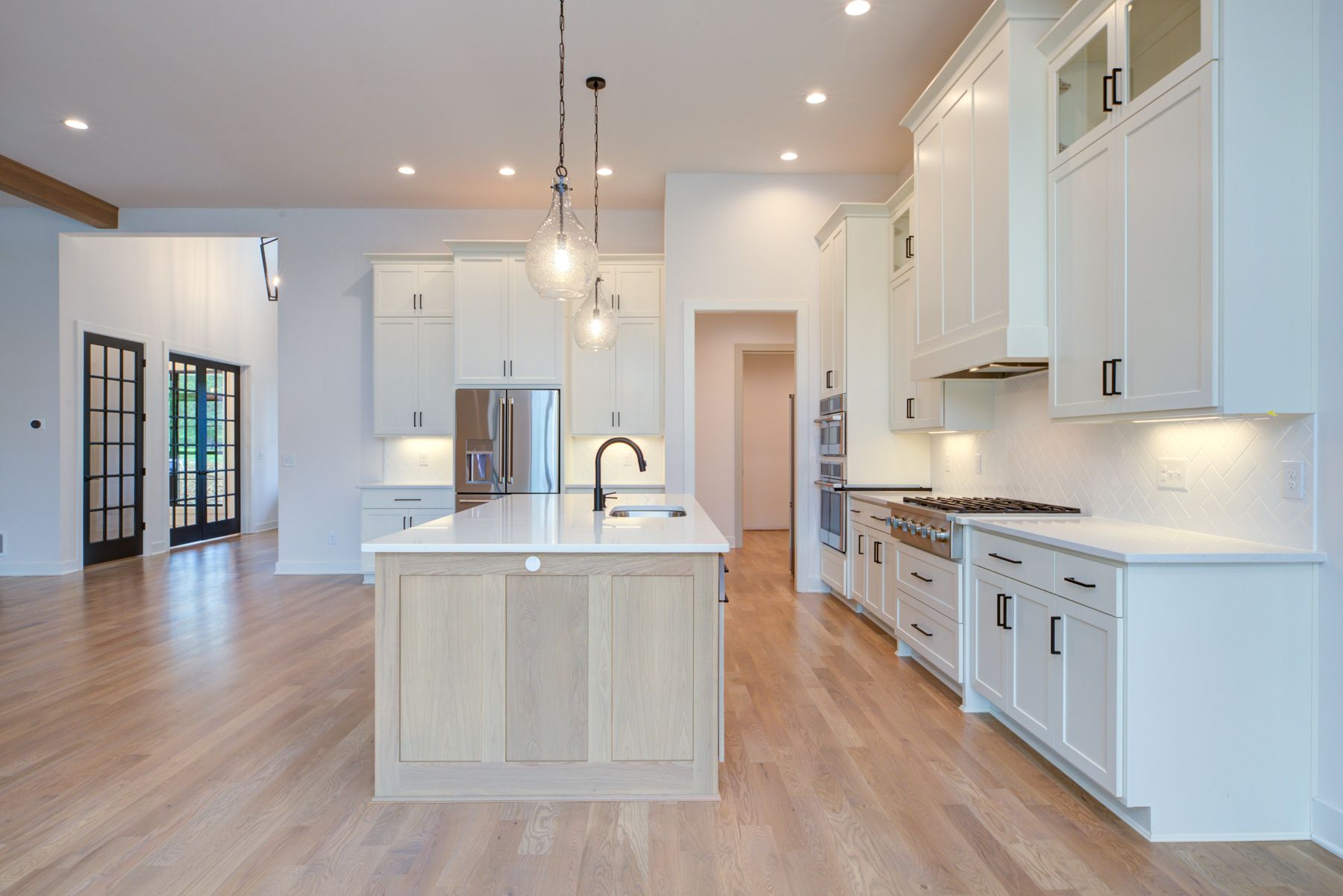 Spacious, modern kitchen with white cabinets, light wood island and flooring, and stainless steel appliances.