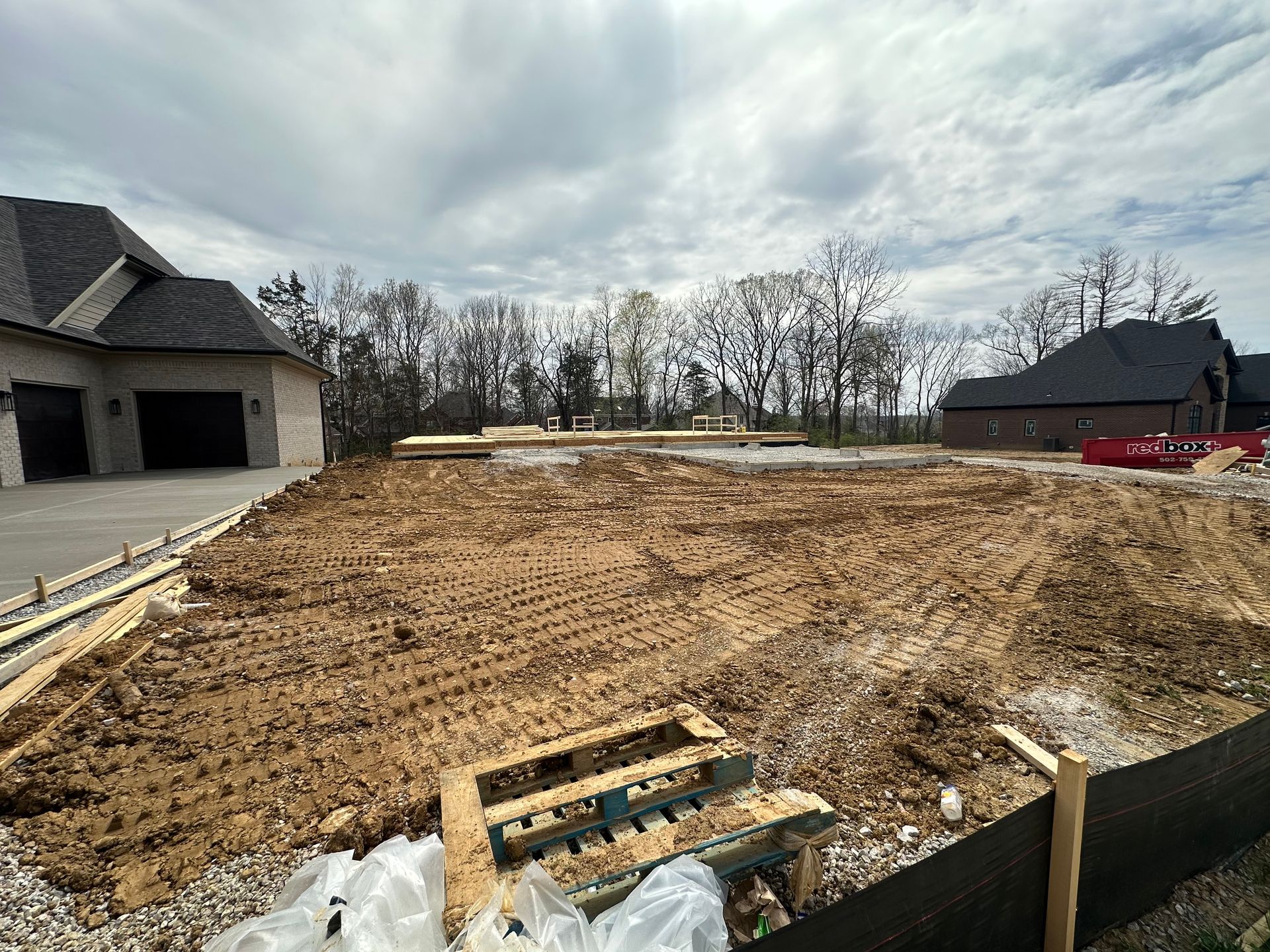 A construction site with a house in the background and a lot of dirt.