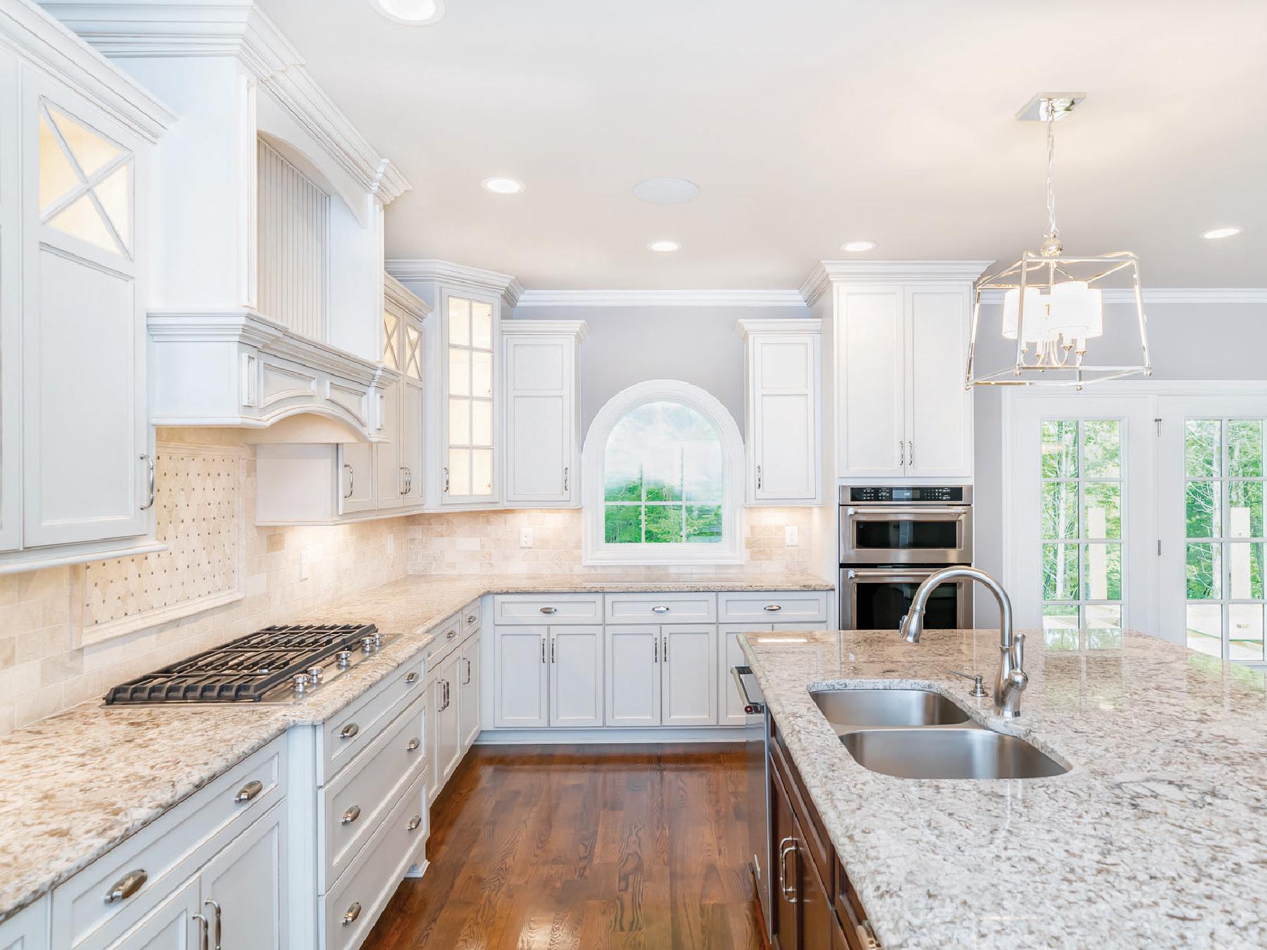 A kitchen with white cabinets , granite counter tops , a stove and a sink.