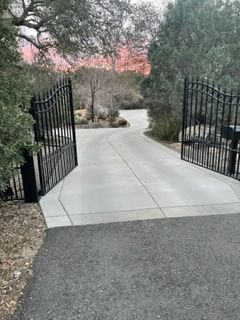 A metal gate is open to a driveway with trees in the background