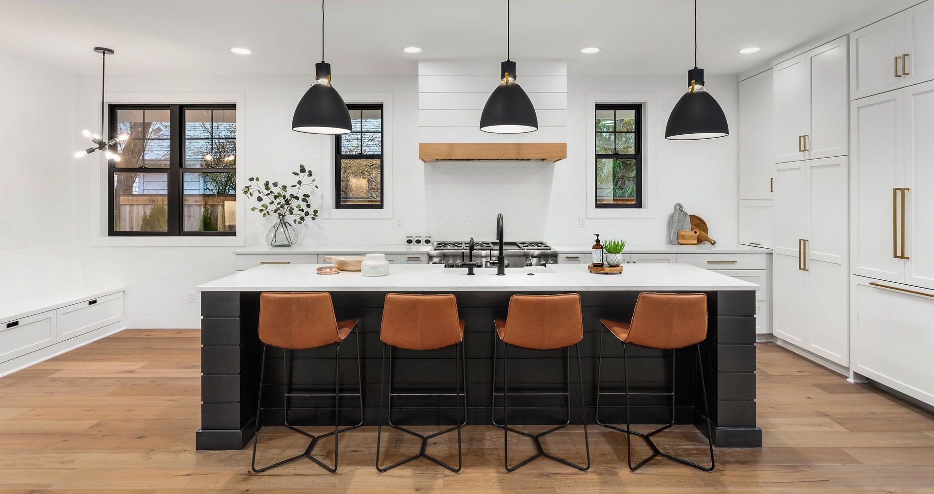 Cuisine moderne avec îlot central noir, plans de travail blancs et tabourets de bar en cuir.