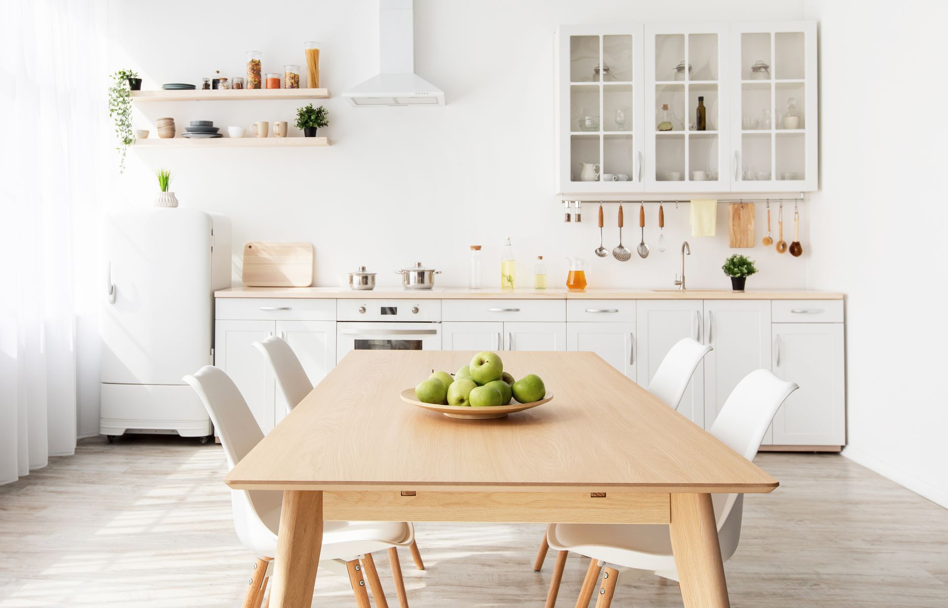Cuisine d'un blanc éclatant avec une table en bois sur laquelle sont posées des pommes vertes, entourée de quatre chaises.