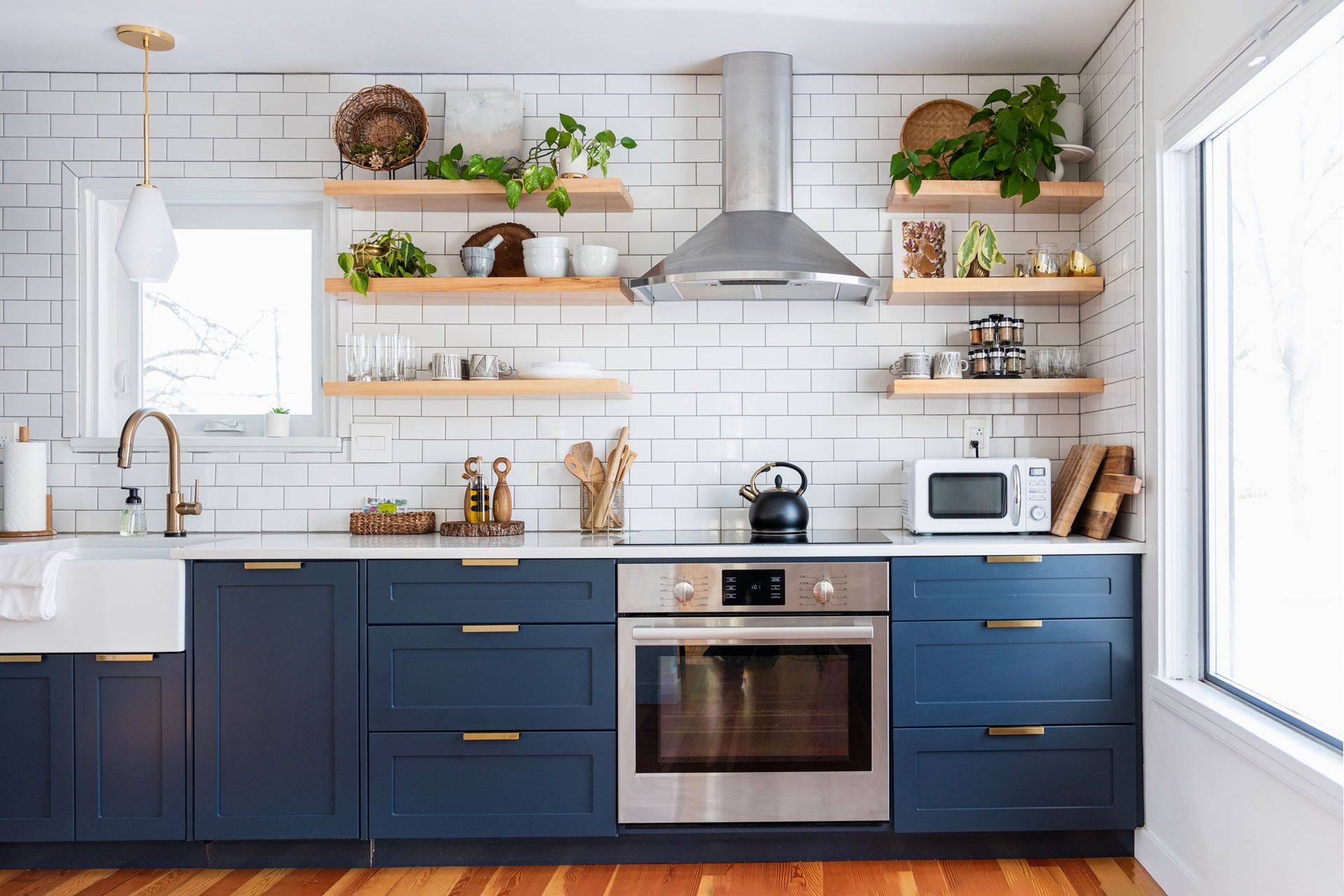A modern kitchen with blue cabinets, stainless steel appliances, open shelves, and white tiles.