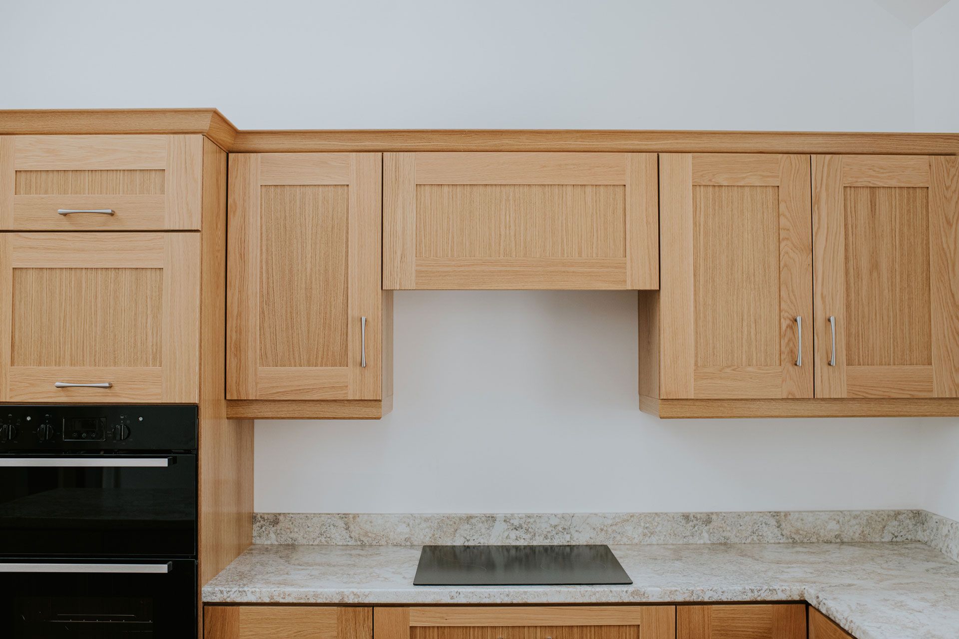 A kitchen with wood cabinets, a marble countertop, and a black oven.